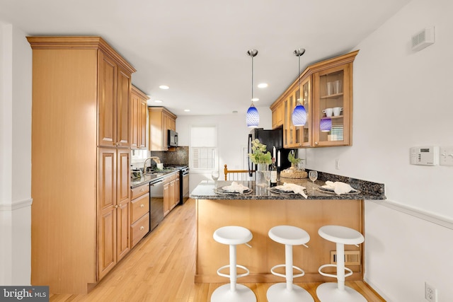 kitchen with stainless steel appliances, a peninsula, light wood-style floors, a kitchen breakfast bar, and dark stone countertops