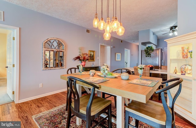 dining area featuring visible vents, light wood-style flooring, ceiling fan, a textured ceiling, and baseboards