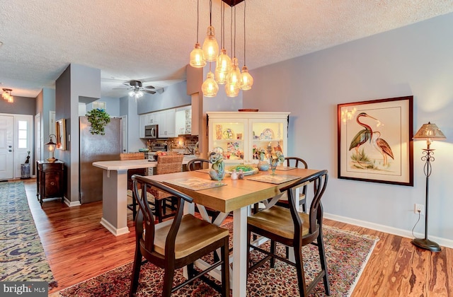 dining area with a textured ceiling, wood finished floors, and baseboards