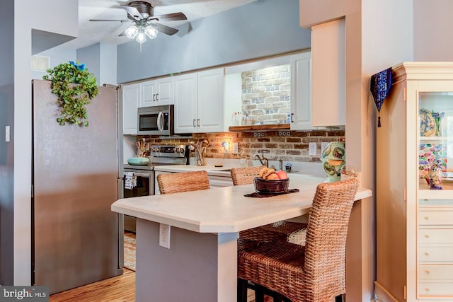 kitchen with a peninsula, a kitchen breakfast bar, white cabinets, light countertops, and appliances with stainless steel finishes