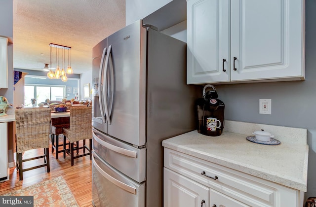 kitchen with light wood-type flooring, stainless steel fridge, white cabinetry, and a textured ceiling