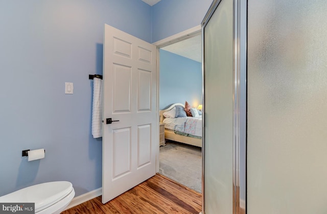 bathroom featuring toilet, baseboards, wood finished floors, and ensuite bathroom