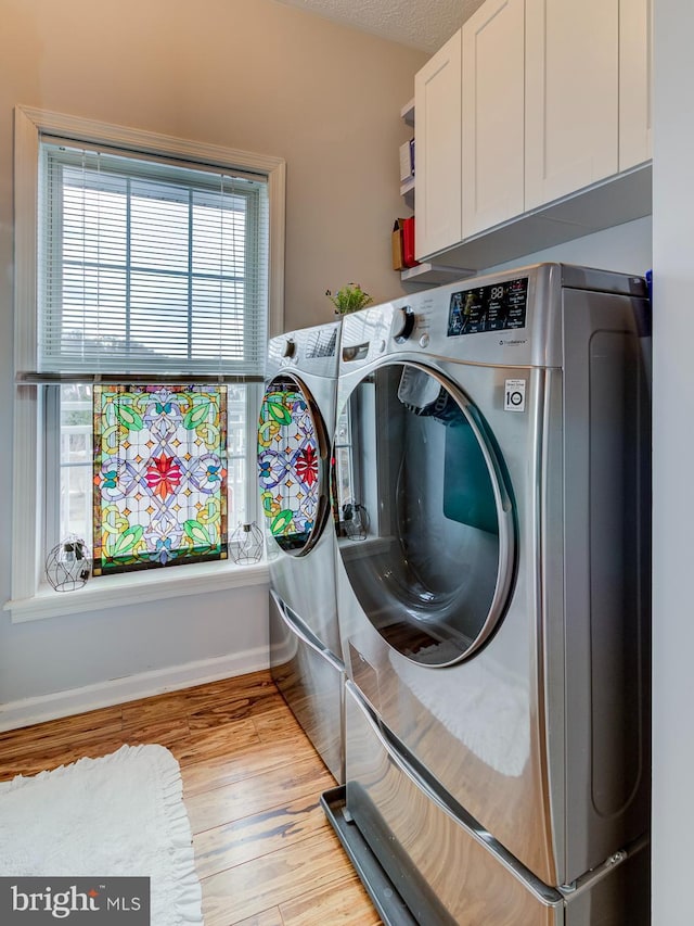 clothes washing area featuring cabinet space, baseboards, washer and clothes dryer, a textured ceiling, and light wood-type flooring