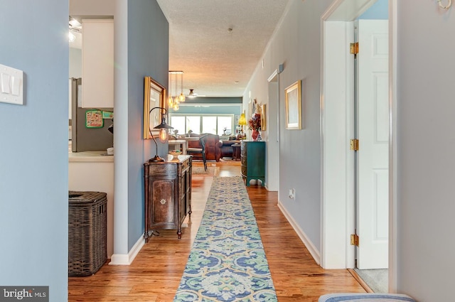 hall with light wood-style floors, a textured ceiling, and baseboards