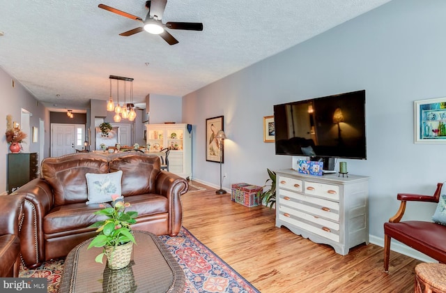 living area featuring light wood-type flooring, a textured ceiling, baseboards, and ceiling fan with notable chandelier