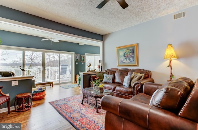 living room featuring a textured ceiling, wood finished floors, visible vents, and a ceiling fan