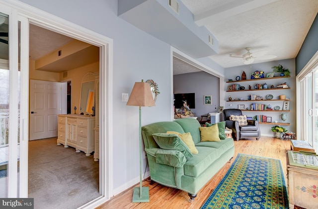 interior space with a ceiling fan, visible vents, a textured ceiling, and wood finished floors