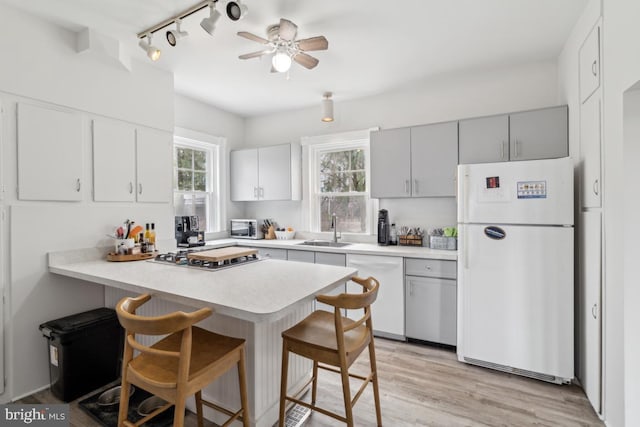 kitchen with a peninsula, a sink, light wood-style floors, appliances with stainless steel finishes, and a kitchen bar