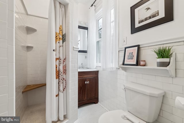 bathroom featuring toilet, a tile shower, tile walls, and vanity