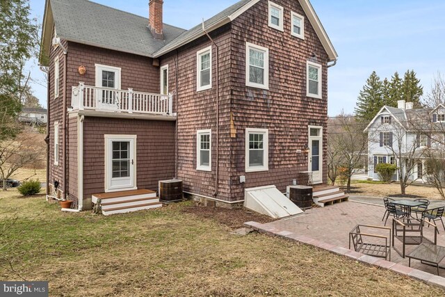 back of property featuring entry steps, a lawn, a balcony, a chimney, and central AC