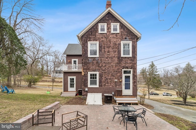 rear view of house featuring entry steps, a balcony, central AC, a yard, and a chimney