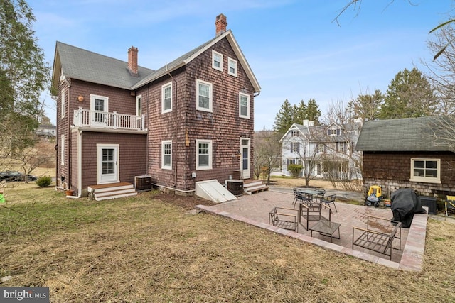 back of house featuring entry steps, a balcony, central air condition unit, a yard, and a chimney