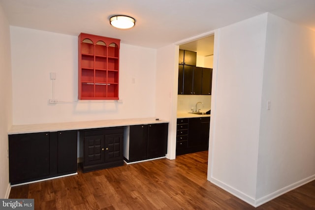 bar with dark wood-style flooring, a sink, and baseboards