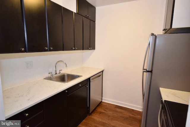 kitchen featuring baseboards, dark wood-style floors, stainless steel appliances, dark cabinetry, and a sink