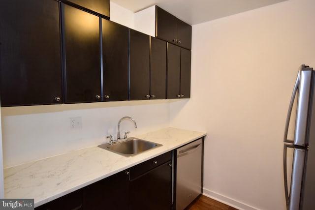 kitchen with light stone counters, freestanding refrigerator, a sink, dishwasher, and baseboards