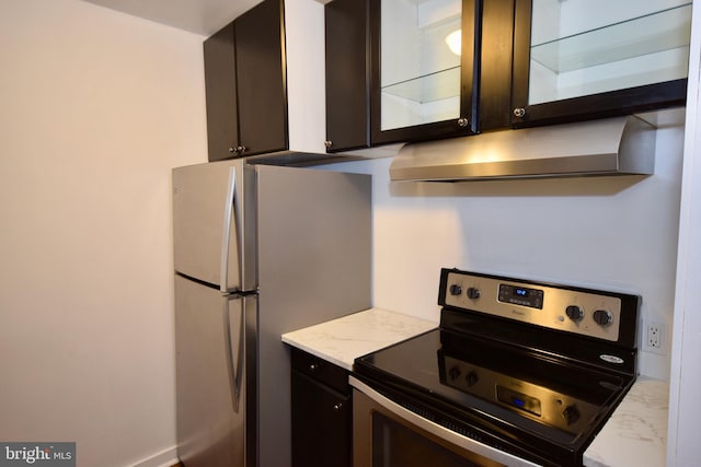 kitchen featuring glass insert cabinets, light stone counters, freestanding refrigerator, stainless steel range with electric cooktop, and under cabinet range hood