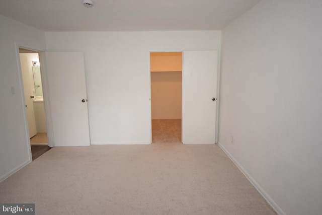 unfurnished bedroom featuring light carpet, a spacious closet, and baseboards