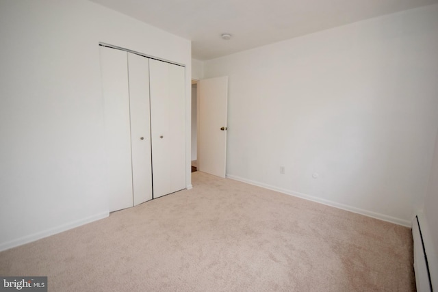 unfurnished bedroom featuring carpet, a baseboard radiator, baseboards, and a closet