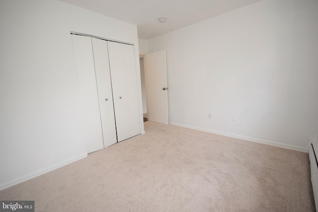 unfurnished bedroom featuring baseboards, a closet, baseboard heating, and light colored carpet