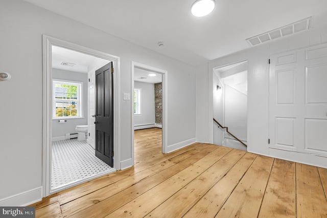 interior space featuring a baseboard heating unit, baseboards, visible vents, and light wood-style floors