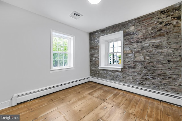 empty room featuring baseboard heating, wood-type flooring, and visible vents