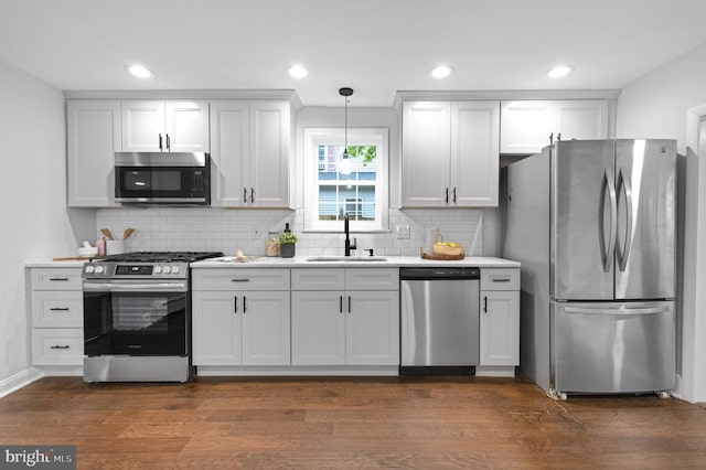 kitchen featuring dark wood finished floors, decorative backsplash, stainless steel appliances, light countertops, and a sink