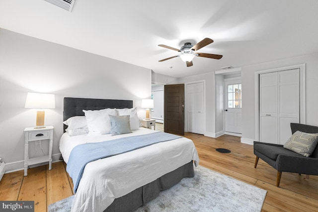 bedroom with light wood finished floors, visible vents, baseboards, and two closets