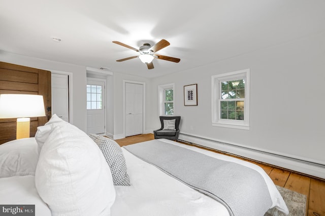 bedroom with multiple closets, a ceiling fan, a baseboard heating unit, and wood finished floors