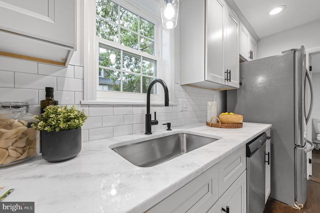 kitchen with tasteful backsplash, white cabinets, light stone countertops, stainless steel dishwasher, and a sink