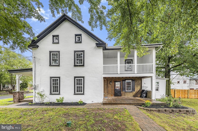 view of front facade featuring fence, a balcony, a front lawn, and stucco siding