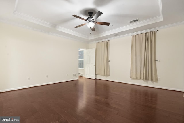 empty room with dark wood-type flooring, visible vents, a raised ceiling, and ornamental molding