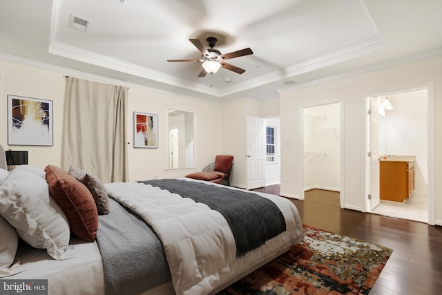 bedroom featuring ornamental molding, a raised ceiling, a walk in closet, and hardwood / wood-style floors