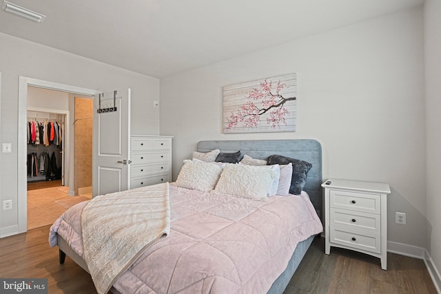 bedroom featuring dark wood-style flooring, visible vents, a spacious closet, and baseboards