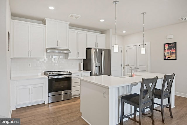 kitchen featuring appliances with stainless steel finishes, a center island with sink, under cabinet range hood, and wood finished floors