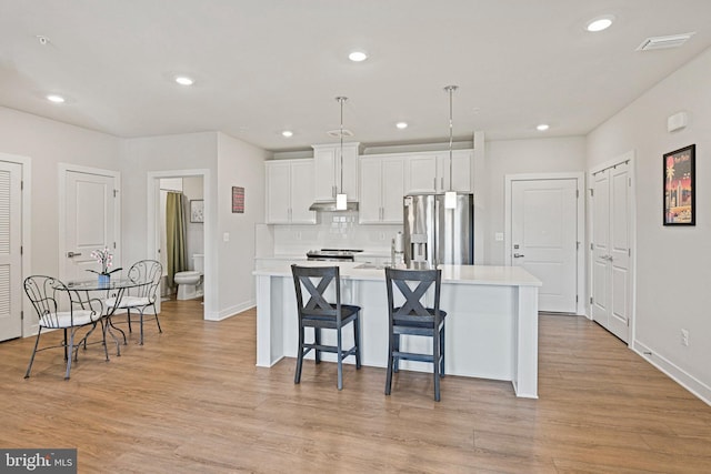 kitchen with under cabinet range hood, stainless steel appliances, white cabinets, light countertops, and an island with sink