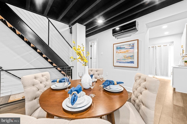 dining area featuring wood finished floors, an AC wall unit, beam ceiling, and stairs