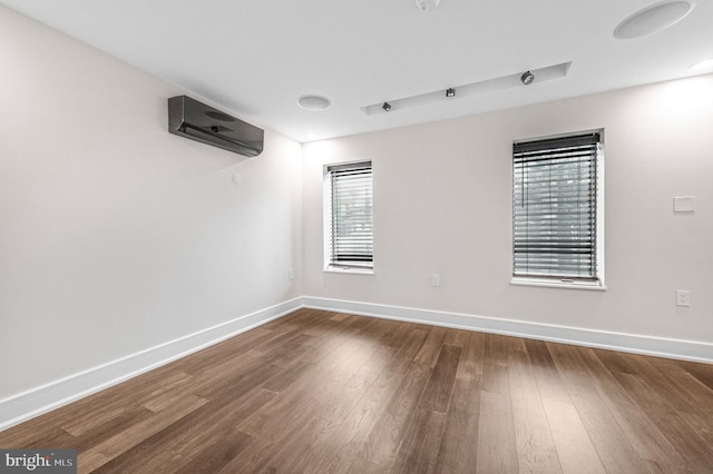 empty room with dark wood-style flooring, a wall mounted AC, and baseboards