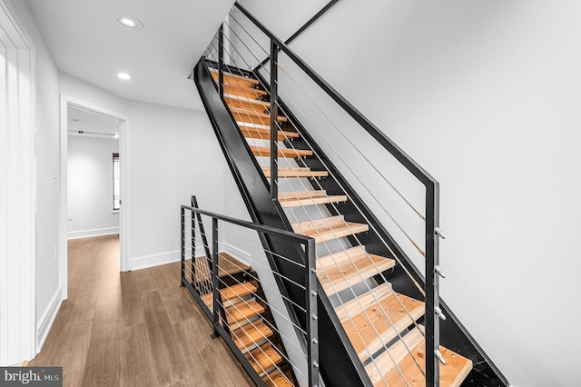 staircase featuring baseboards, wood finished floors, and recessed lighting