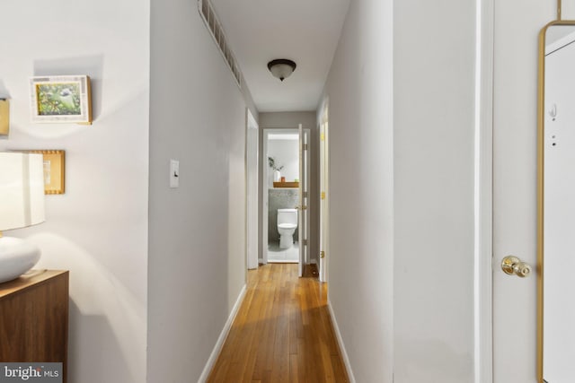 hall with hardwood / wood-style flooring, baseboards, and visible vents