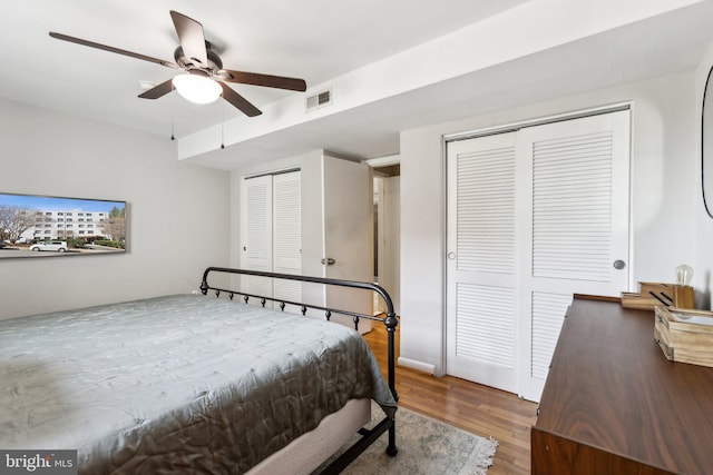 bedroom with visible vents, a ceiling fan, multiple closets, and wood finished floors