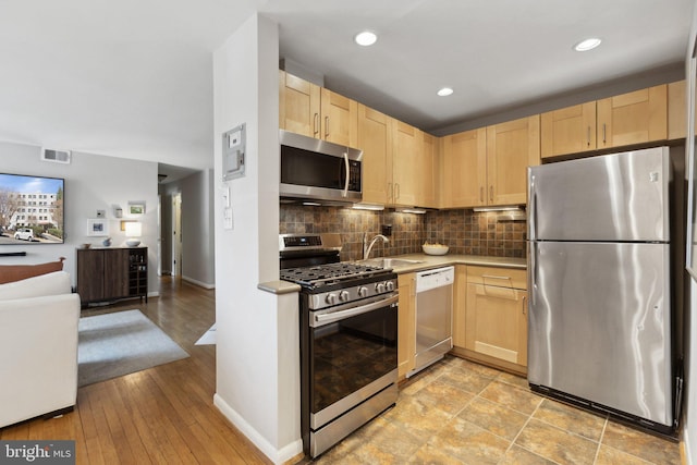 kitchen featuring light brown cabinets, a sink, tasteful backsplash, open floor plan, and appliances with stainless steel finishes