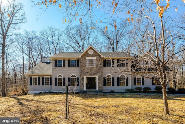 colonial-style house featuring stone siding, a chimney, and a front lawn