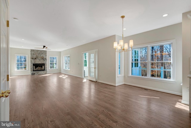 unfurnished living room with recessed lighting, an inviting chandelier, a stone fireplace, wood finished floors, and baseboards