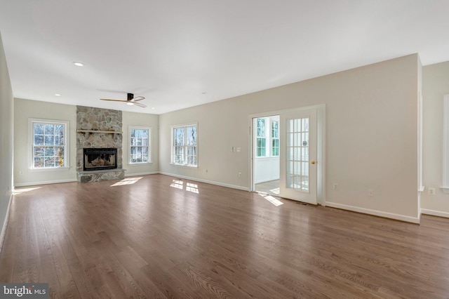 unfurnished living room featuring a healthy amount of sunlight, baseboards, wood finished floors, and a stone fireplace