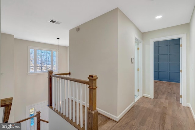 hallway featuring baseboards, visible vents, light wood finished floors, and an upstairs landing