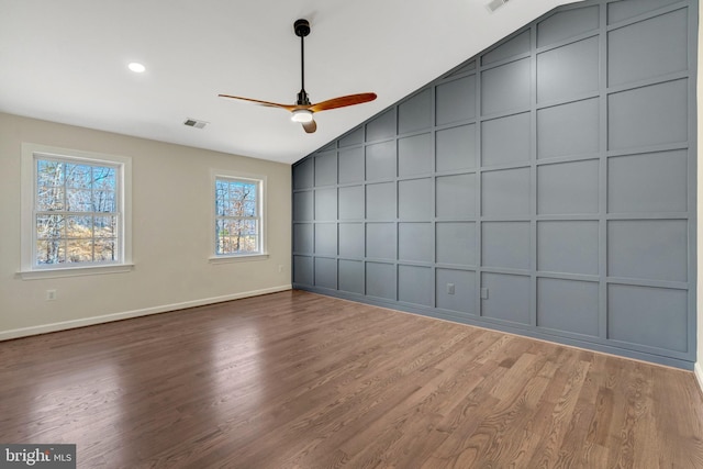 unfurnished room featuring visible vents, a decorative wall, a ceiling fan, vaulted ceiling, and wood finished floors