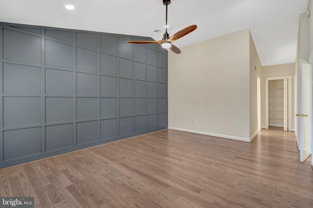 interior space featuring baseboards, a ceiling fan, wood finished floors, vaulted ceiling, and a decorative wall