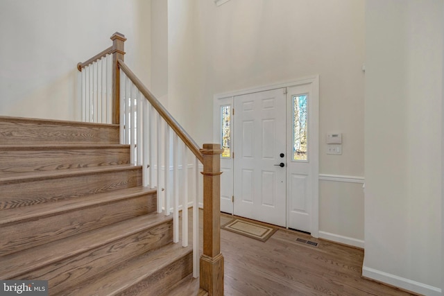 foyer entrance featuring visible vents, baseboards, stairs, a high ceiling, and wood finished floors