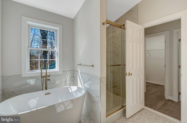 bathroom featuring a soaking tub, a shower stall, a walk in closet, and tile walls