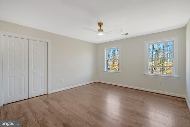 unfurnished bedroom featuring ceiling fan, wood finished floors, visible vents, baseboards, and a closet